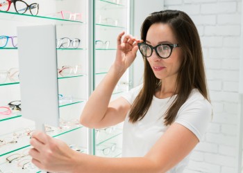 Mujer probándose gafas frente a un espejo en Óptica Jordi Porta.