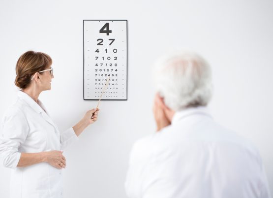 Optometrista realizando examen de agudeza visual a un paciente mayor.