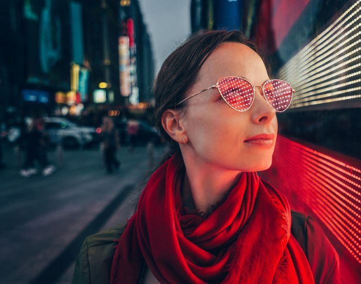 Mujer con gafas de sol con reflejos de luces LED en un entorno urbano nocturno.